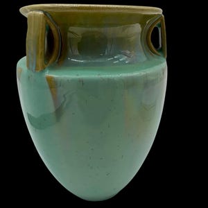 May include: A green ceramic vase with two handles. The vase has a light green glaze with brown accents. The vase is in the shape of an amphora.