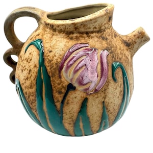 May include: A brown ceramic pitcher with a green and pink floral design. The pitcher has a rounded body and a curved handle.