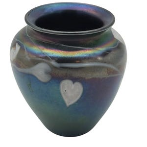 Puede incluir: Un jarrón iridiscente decorativo con interior azul oscuro y borde acampanado. El jarrón presenta diseños blancos en forma de corazón y un degradado de color de azul a verde. La superficie tiene un aspecto texturizado y agrietado.