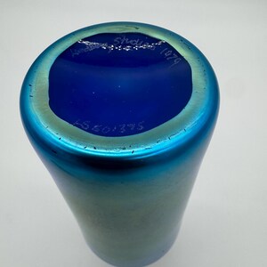 May include: A blue iridescent glass vase with a blue glass base. The base has the text "Am&eacute;d&eacute;e Studio 1974" written in white.