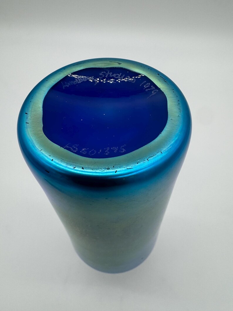 May include: A blue iridescent glass vase with a blue glass base. The base has the text "Am&eacute;d&eacute;e Studio 1974" written in white.