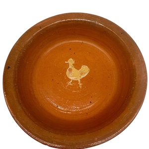 May include: A terracotta bowl with a hand-painted yellow chicken design. The bowl is round and has a slightly raised rim.