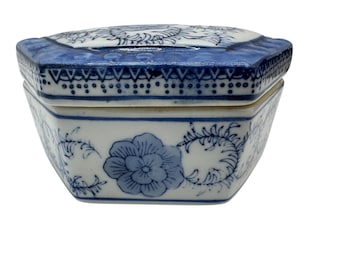 May include: A blue and white porcelain trinket box with a hexagonal shape. The lid and body are decorated with floral and scroll patterns. The lid has a blue border with a detailed design. The box is a decorative storage item.