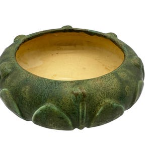 May include: A green ceramic bowl with a textured surface and a yellow interior. The bowl has a rounded shape with a raised rim and a decorative design.