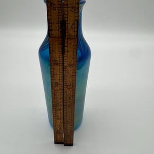 May include: A small blue iridescent glass vase with a narrow neck and a rounded body. The vase is approximately 6 inches tall.