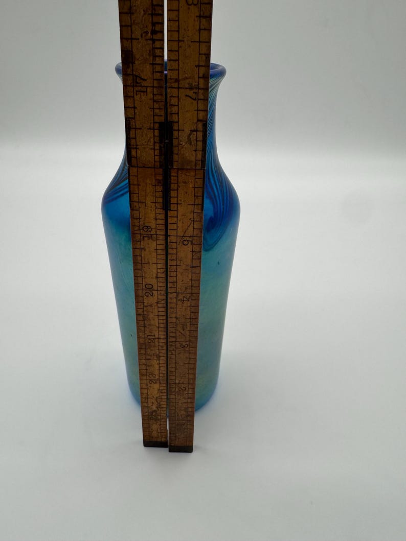 May include: A small blue iridescent glass vase with a narrow neck and a rounded body. The vase is approximately 6 inches tall.