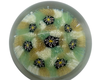 May include: A clear glass paperweight with a swirling pattern of green, white, and gold. The paperweight features a design of small, multi-colored flowers.