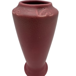 Könnte beinhalten: Eine tiefrote Keramikvase mit einer strukturierten Oberfläche und einer leicht ausgestellten Öffnung. Die Vase hat ein schlichtes, elegantes Design mit dezenten Reliefdetails am Rand.