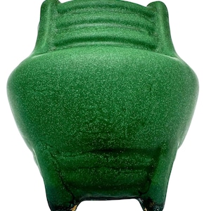 Può includere: Un vaso di ceramica verde con una superficie strutturata. Il vaso ha un corpo arrotondato, un bordo svasato e tre piedini. Il colore è un verde vibrante e screziato.