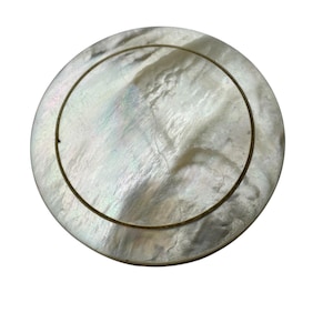 Op de afbeelding: Een ronde, iriserende parelmoeren plaat met een dunne, goudkleurige rand. De plaat heeft een natuurlijk, getextureerd oppervlak met subtiele kleurvariaties, dat licht reflecteert. Het ontwerp is eenvoudig en elegant.