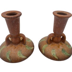 May include: A pair of brown ceramic candle holders with green and brown glaze. The holders have a round base and a tall, cylindrical top.