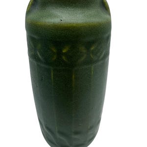 May include: A tall, dark green ceramic vase with a textured surface. The vase has a cylindrical shape with a slightly flared top and decorative embossed patterns around the middle. The overall design is simple and elegant.