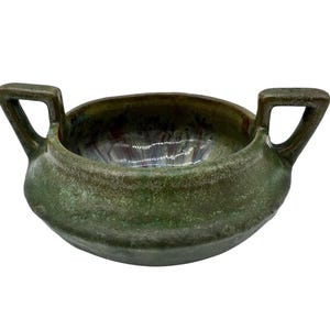 Może przedstawiać: Okrągła ceramiczna miska z dwoma kanciastymi uchwytami po przeciwnych stronach. Zewnętrzna część posiada teksturowaną, nakrapianą zieloną glazurę, podczas gdy wnętrze wykazuje błyszczące wykończenie z mieszanką odcieni fioletu, błękitu i zieleni.
