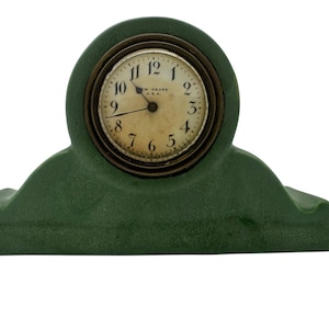 May include: A green ceramic clock with a round, white face and black Roman numeral markings. The clock face also includes the text "New Haven, U.S.A."