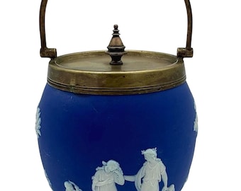 May include: A blue and white ceramic cookie jar with a brass lid and handle. The jar features a white cameo design of figures in a pastoral scene.