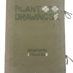 May include: An aged green book titled "PLANT DRAWINGS" with white floral details and the text "NEWCOMB COLLEGE." The book is bound with a string tie and shows signs of wear.