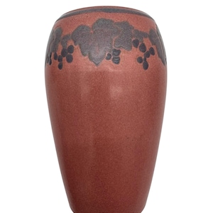 May include: A tall, terracotta-colored vase with a speckled finish. The upper portion features a dark gray grape leaf and cluster design. The vase has a slightly flared top and a smooth, rounded body, suitable for home decor.