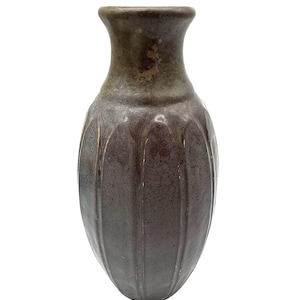 May include: A tall, brown ceramic vase with a textured, crackled surface. The vase has a rounded body with vertical ridges and a narrower neck. The color gradient transitions from a darker brown at the base to a lighter, olive-toned brown at the top.