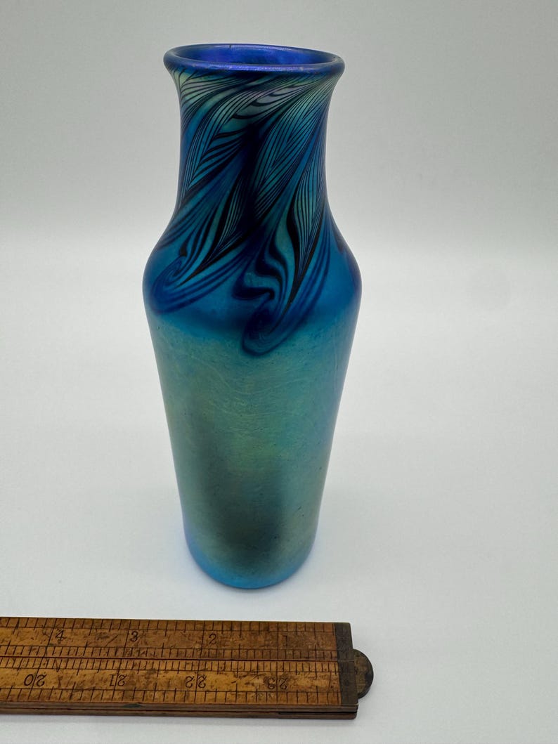May include: A blue iridescent glass vase with a feathered pattern. The vase is approximately 6 inches tall.