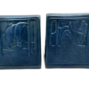 May include: Two navy blue bookends with a rectangular shape. Each bookend features a raised relief design of a sailboat. The bookends are made of a solid material and are suitable for holding books.