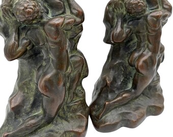 May include: Pair of bronze bookends depicting figures in a classical style. The figures are nude and appear to be struggling. The bronze has a dark brown patina with green highlights, and the bookends are set against a white background.