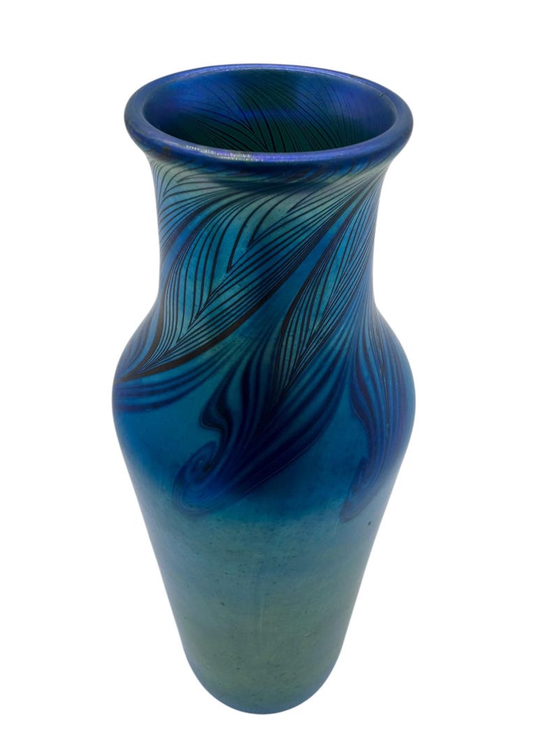 May include: A blue glass vase with a swirling, feathered pattern. The vase has a narrow neck and a wide base.