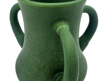 May include: A green ceramic vase with two curved handles. The vase has a textured surface and a wide opening. The handles are attached to the sides of the vase, and the color is a deep, earthy green.