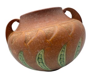 May include: A brown ceramic vase with two handles and a green peapod design. The vase has a textured surface and is decorated with a repeating pattern of peapods.