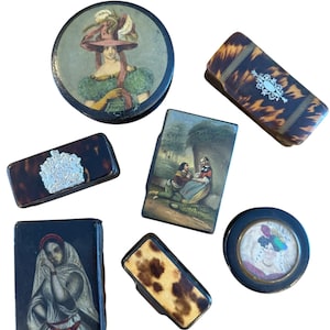 Pode incluir: Uma coleção de caixas e estojos decorativos antigos. Os itens apresentam retratos pintados de mulheres, paisagens e padrões decorativos. As caixas têm várias formas, incluindo redondas e retangulares, e são feitas de materiais como tartaruga.