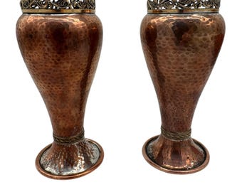 May include: A pair of hammered copper vases with silver accents. The vases have a flared base and a narrow neck. The silver accents are around the top and bottom of the vases.