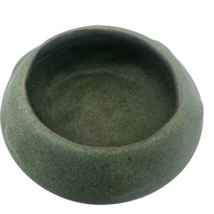 Puede incluir: Un cuenco de cerámica verde con una superficie rugosa y texturizada. El cuenco es redondo y tiene una abertura ancha y poco profunda.