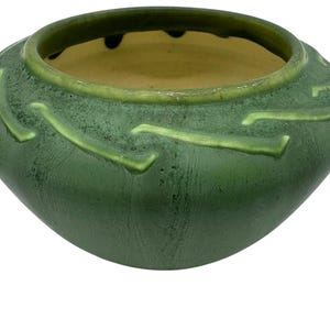 May include: A green ceramic bowl with a textured surface and a lighter green rim. The bowl has a rounded shape with a wide opening and decorative, raised, curved lines around the exterior. The interior is a light yellow color.