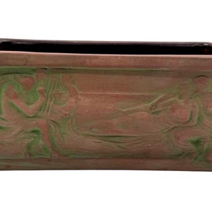 May include: Rectangular terracotta planter with a dark interior. The exterior features a bas-relief design of classical figures in shades of green. The planter is ideal for displaying plants and flowers.