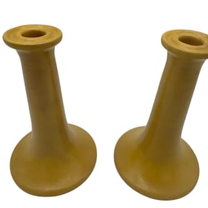 Könnte beinhalten: Ein Paar gelbe Kerzenhalter aus Keramik mit einem ausgestellten Sockel und einem zylindrischen Oberteil.
