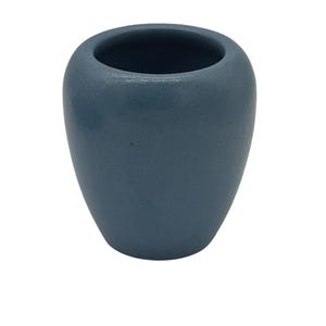 Könnte beinhalten: Eine kleine blaue Vase mit strukturierter Oberfläche. Die Vase hat einen abgerundeten Körper und eine breite Öffnung oben. Die Farbe ist ein gedämpftes, staubiges Blau. Die Vase ist wahrscheinlich aus Keramik oder Steinzeug.