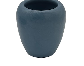 May include: A small, blue vase with a textured surface. The vase has a rounded body and a wide opening at the top. The color is a muted, dusty blue. The vase is likely ceramic or stoneware.