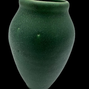 May include: A dark green ceramic vase with a rounded bottom and a slightly flared opening. The vase has a textured surface and a speckled appearance.