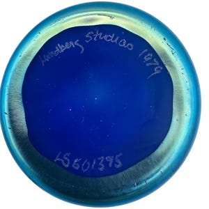 May include: A blue glass vase with an iridescent finish. The bottom of the vase is marked with "Hultberg Studio 1979" and a number "15601395".