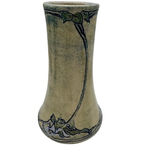 May include: A beige ceramic vase with a flared base and a slightly curved body. The vase features a dark green and black floral design that wraps around the body. The top rim has a dark green accent.