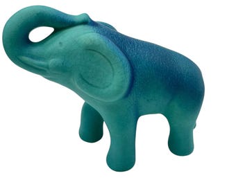 May include: A ceramic elephant figurine in shades of teal and blue. The elephant has a raised trunk and is standing on four legs. The figurine has a textured surface and is a decorative item.