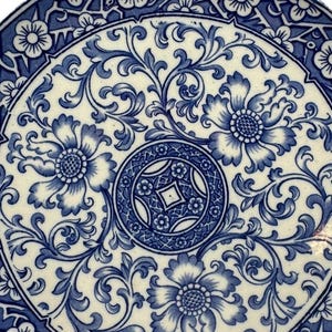 May include: A round, white ceramic plate with a blue floral design. The plate features a central medallion and a border of flowers and leaves. The intricate pattern is a classic, elegant design.