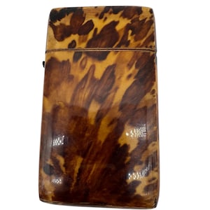 May include: A rectangular case featuring a glossy, mottled brown and tan tortoiseshell pattern. The object has a smooth, polished surface with a horizontal seam dividing the top lid from the main body, showcasing a classic, uniform design.