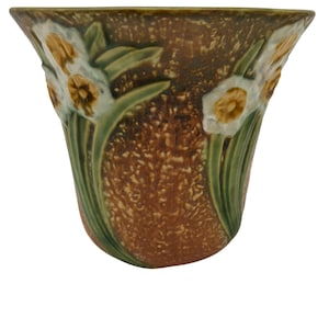 May include: A brown and green ceramic vase with a floral design of white and yellow daffodils. The vase has a textured surface and a flared rim.