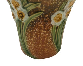 May include: A brown and green ceramic vase with a floral design of white and yellow daffodils. The vase has a textured surface and a flared rim.