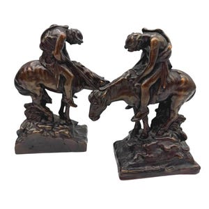 May include: Two bronze sculptures depict a person riding a horse. The figures are detailed, with the rider leaning forward. The sculptures are mounted on a textured base, showcasing a classic equestrian theme.