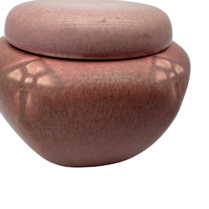 May include: A pink ceramic lidded jar with a floral design. The jar has a textured surface and a rounded shape.