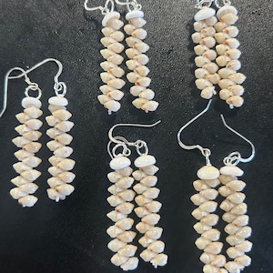 May include: A set of six long, silver earrings with white shell beads. The earrings are arranged in three pairs, with each pair having a slightly different length.