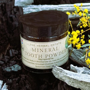 May include: A dark brown jar of The Herbal Estate Mineral Tooth Powder with a cream-coloured label. The label displays the text 50g Ingredients: Bentonite Clay, Sodium Bicarbonate, Bio Activated Carbon, Hydroxapatite, Activated Charcoal, Xylitol, Peppermint and Spearmint Essential Oil.