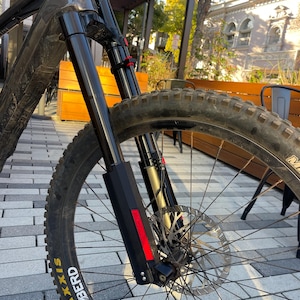 May include: A black mountain bike with a front suspension fork and a black Maxxis  'IberD' tire. The bike is parked on a brick patio.