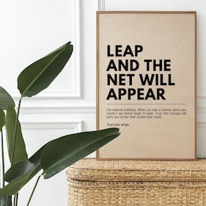 May include: A framed print with the words "LEAP AND THE NET WILL APPEAR" in bold black font. The print has a light brown background and a wooden frame. The text below reads "Life rewards boldness...Trust your wings."